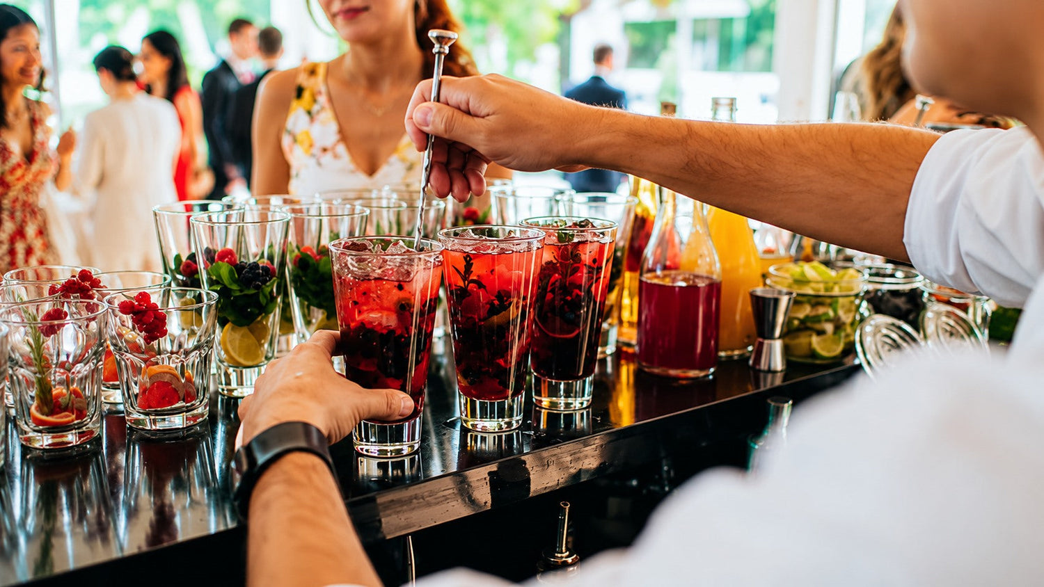 Bartender preparing multiple batched berry cocktails for a party at a bar.