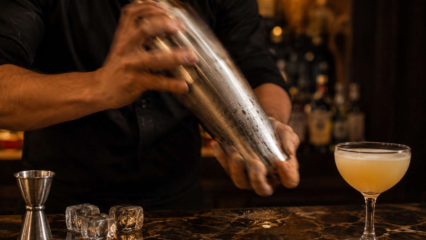 Bartender shaking a cocktail shaker for a shaken cocktail at a home bar