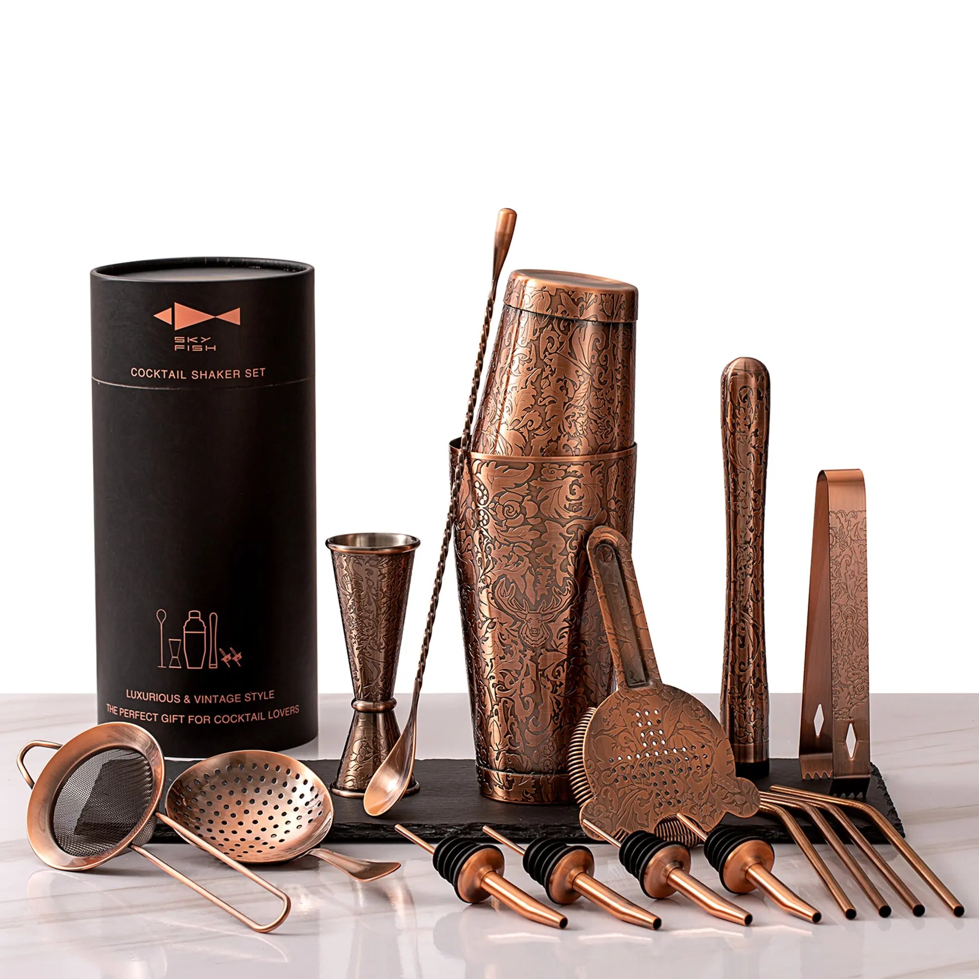 Copper cocktail shaker set with tools and packaging on a white background