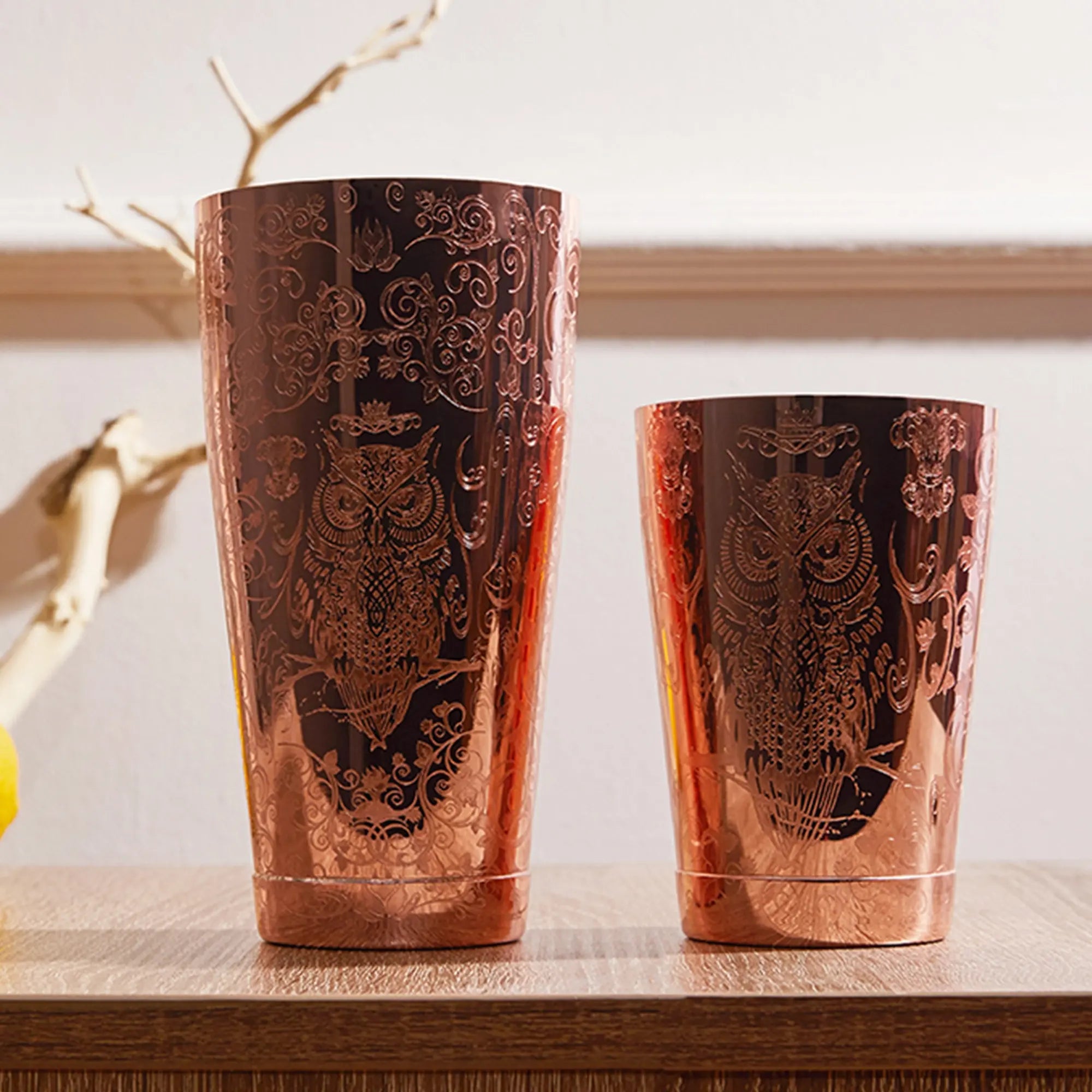 Two copper tumblers with owl designs on a wooden surface.