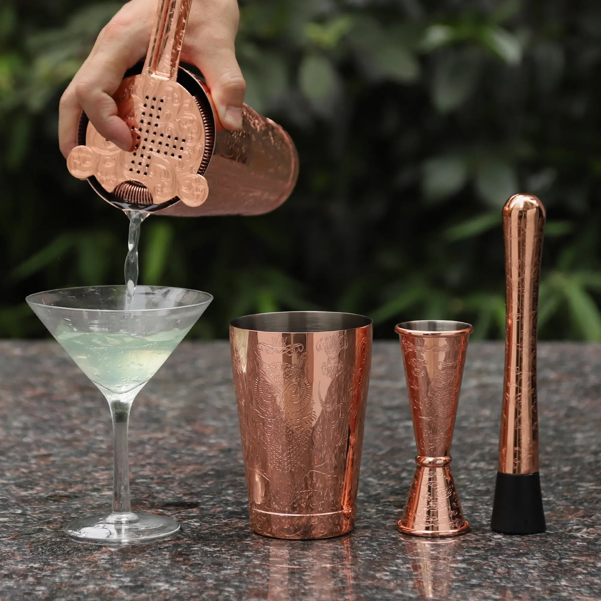 A bartender pouring a cocktail into a glass cup using SKYCORPS 7-piece antique copper etched Boston shaker set with Hawthorne strainer.