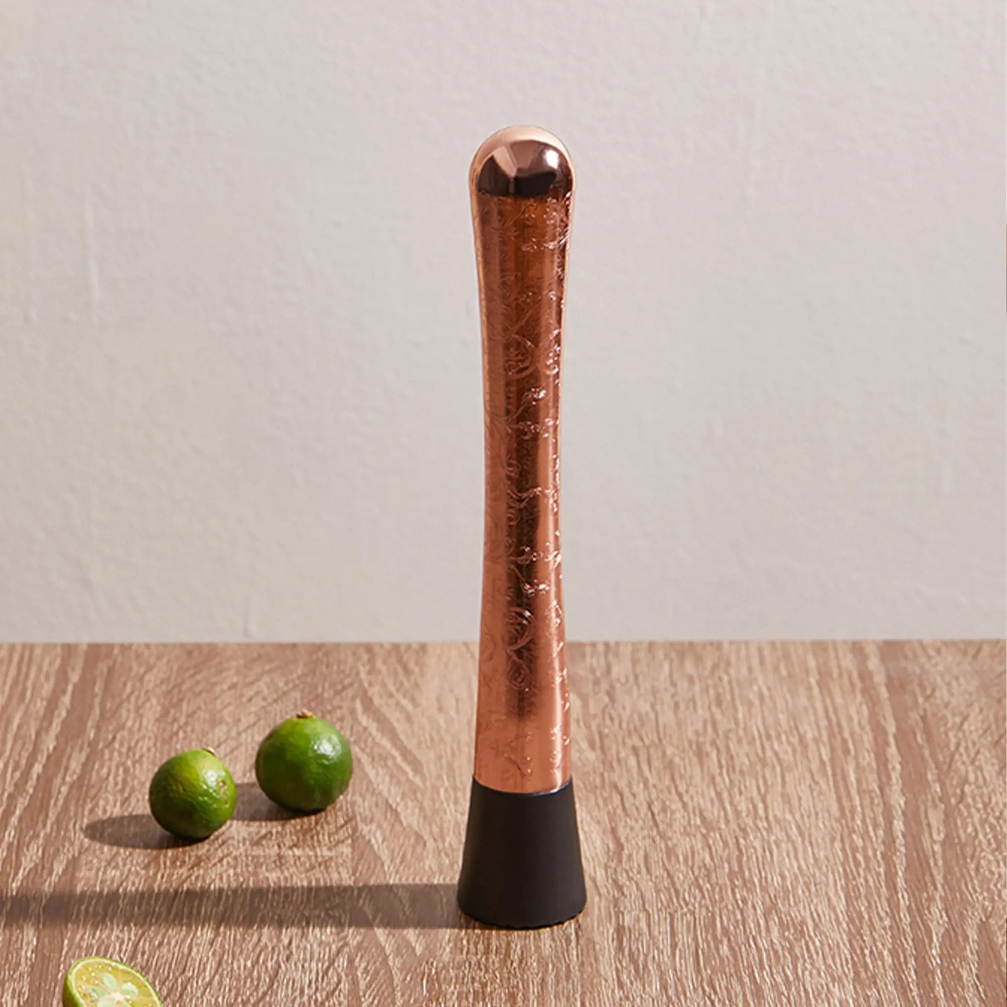 Copper muddler with black bottom on a wooden surface with limes