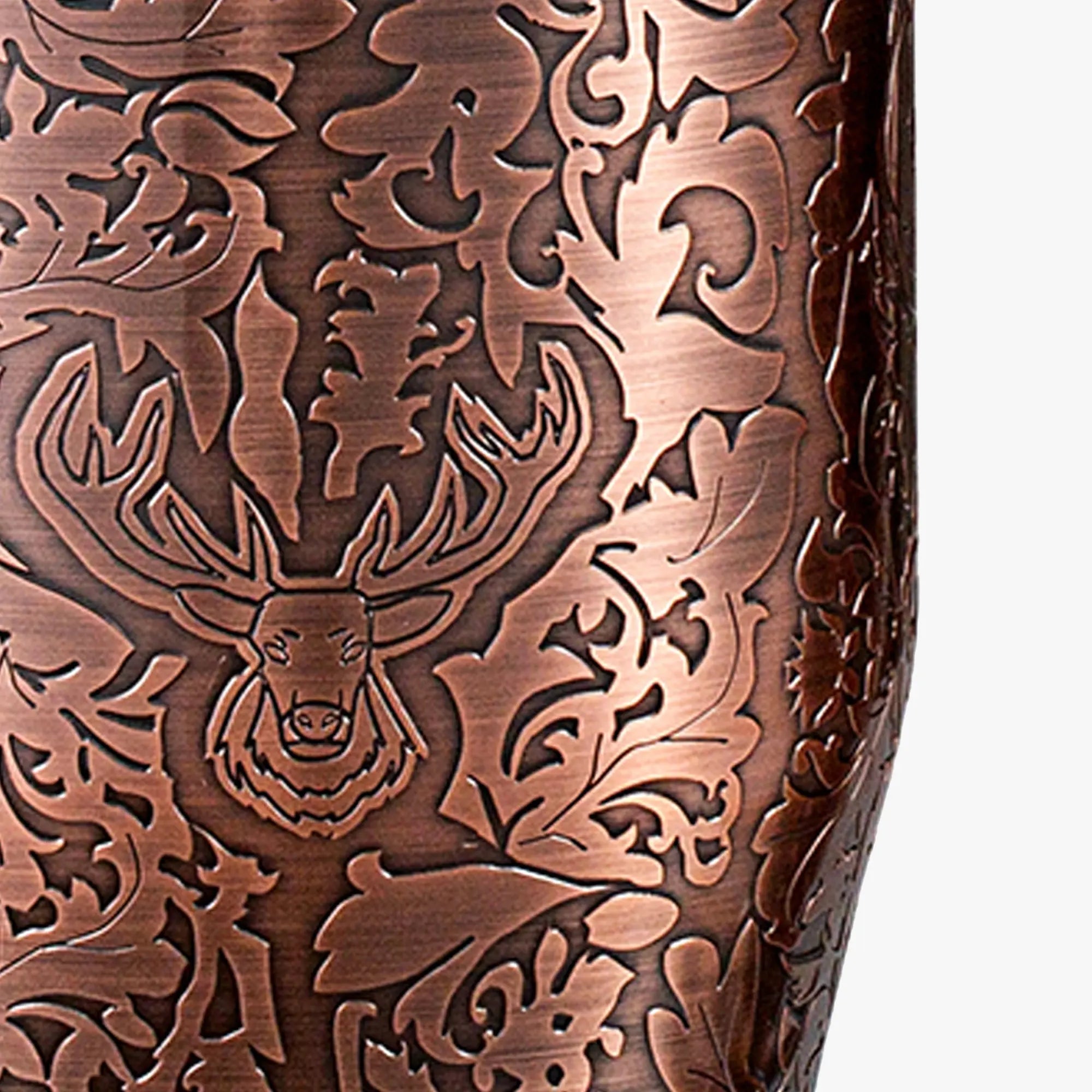 A close-up view of the 3D raised reverse-etched stag head and baroque leaf pattern on an antique copper plated stainless steel cocktail shaker.